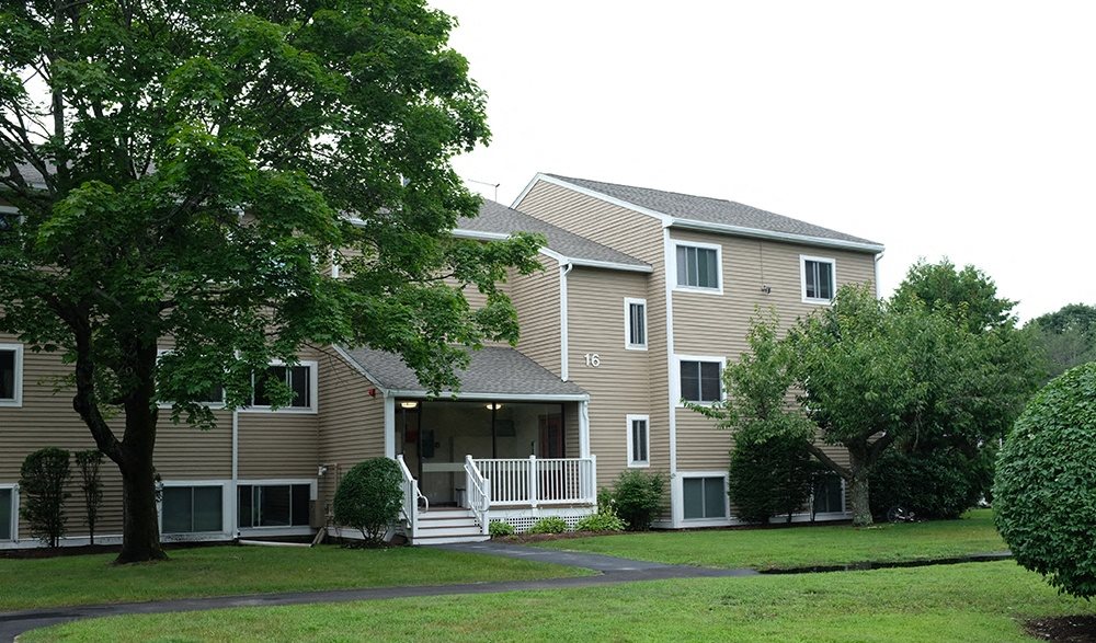 a large apartment complex with a grassy area and trees in front of it